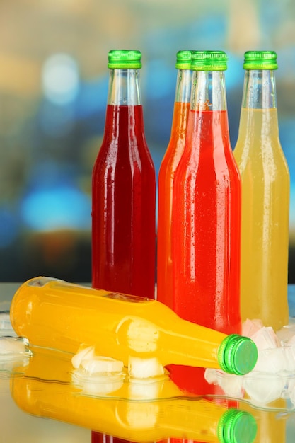 Bottles with tasty drinks with ice cubes on bright background