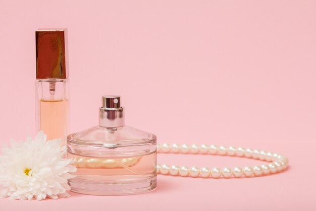 Bottles with women perfume, beads and flower bud in a pink background with copy space. Women products.