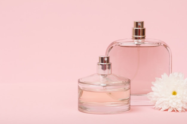 Bottles with women perfume and flower bud in the pink background. Women products.