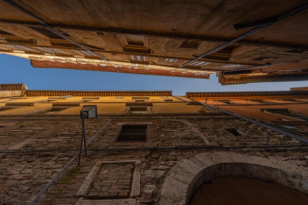 이탈리아 페루자 (Perugia) 의 중세 지역 에 있는 오래된 건물 들 사이 의 어두운  ⁇ 은 거리 에서 아래 로부터 보는 모습