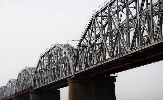 Bottom up view of several spans of a railway truss bridge against a cloudy sky