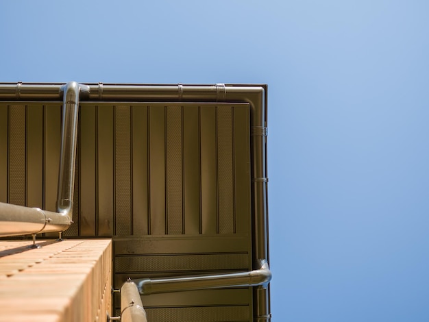 Bottom view of the corner visor of a house with storm drain and blue sky