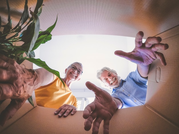 Bottom view of a couple of smiling elderly people moving house and opening packing boxes.