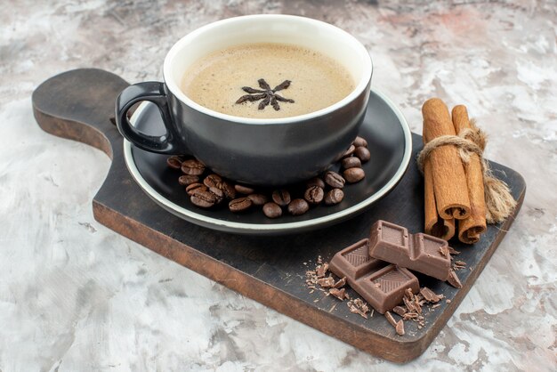 Vista dal basso tazza di caffè aromatizzata con cioccolato all'anice bastoncini di cannella su tavola di legno chicchi di caffè tostati nel piattino sul tavolo