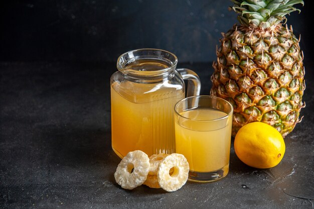 bottom view fresh pineapple juice in glass and carafe lemon dried pineapple slices on dark background