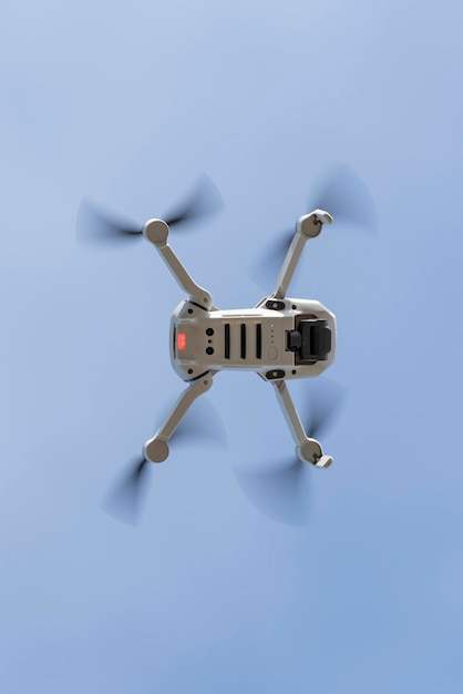 Bottom view of a little grey drone flying with the light blue sky on the background with copy space