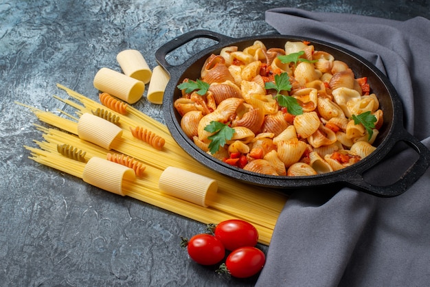 bottom view raw pastas spaghetti rigatoni spirals tasty pasta in frying pan cherry tomatoes on grey background