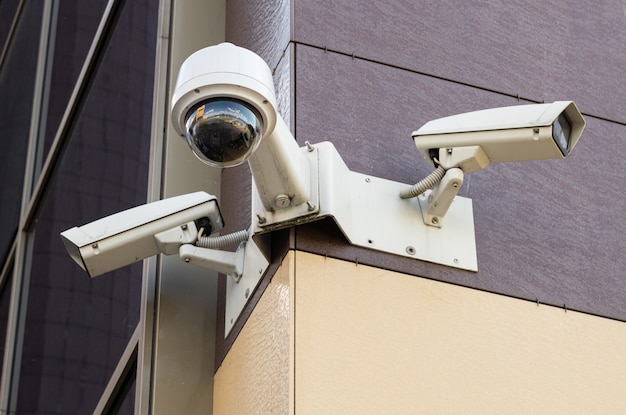 Bottom view of three white surveillance cameras on office building with pale yellow