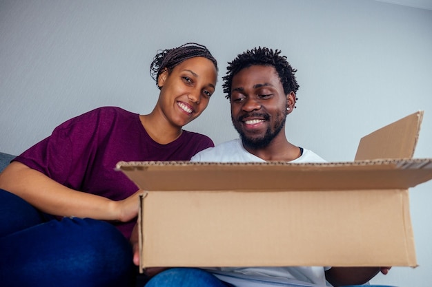 Bottom view of young afro american couple looking through the\
cardboard box on cat or dog inside .