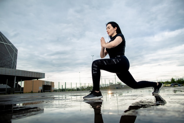 Bottom view, young sporty brunette is training outdoors. Woman makes lunges outdoors. Fitness, workout, sport concept