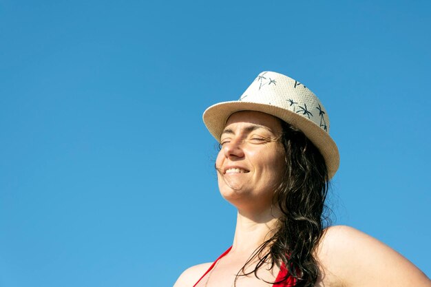 Bottom view of a young woman in a hat and a swimsuit against the background of a blue sky