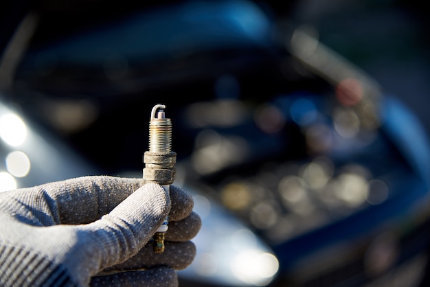 Bougie voor motor in mannenhand, auto met open kap.