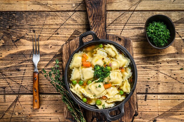 Bouillonsoep met ravioli dumplings pasta in een pan. Houten achtergrond. Bovenaanzicht.