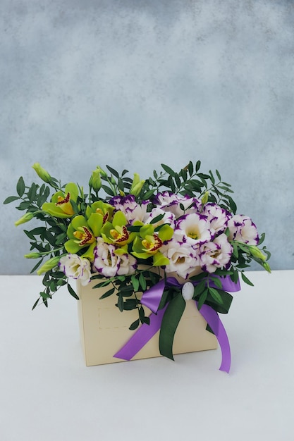 Bouquet of archidea and eustoma in a paper gift box on a gray background In purple white and yellow