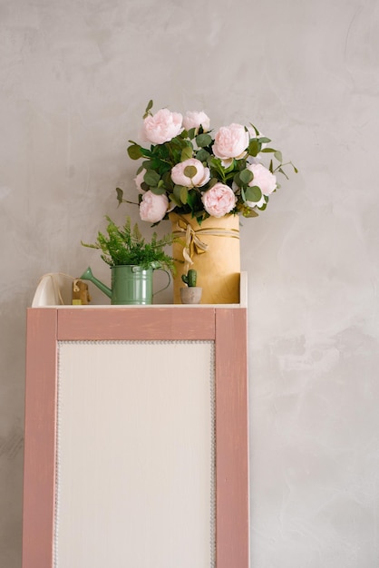 A bouquet of artificial peonies in a vase greenery in a watering can on cabinet in children's room