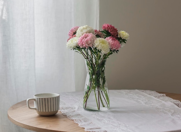 유리 꽃병에 담긴 과꽃 꽃다발, 둥근 테이블 위에 놓인 커피 한 잔