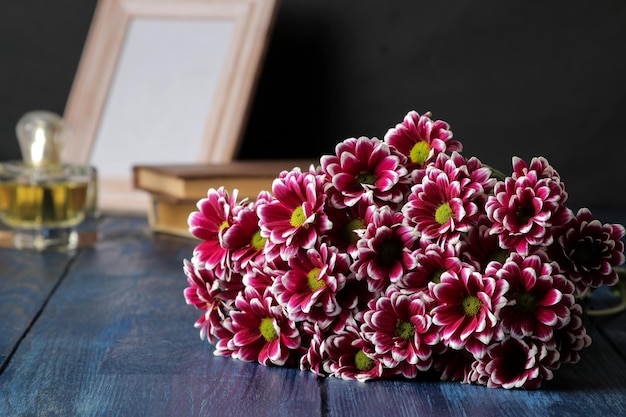 Bouquet di fiori autunnali di crisantemi rosa e una bottiglia di profumo su un tavolo di legno blu