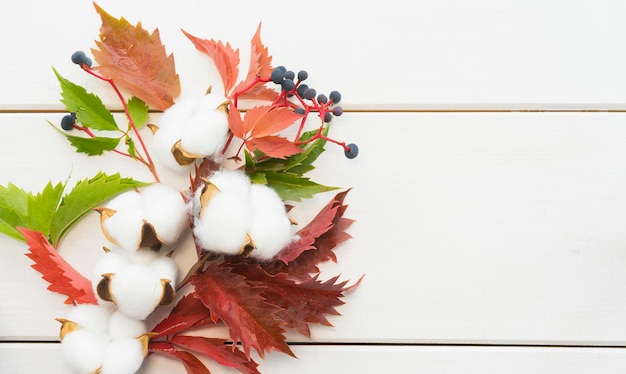 白い木製の背景に秋の葉と綿の花束