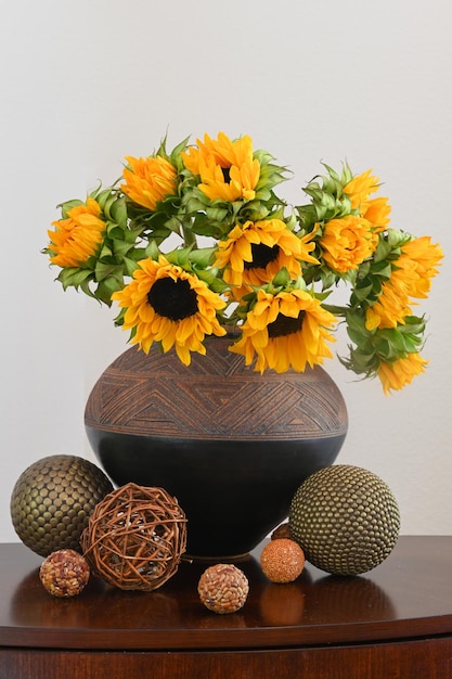 土の花瓶に秋のひまわりの花束。木と金属で作られたボールの形の装飾