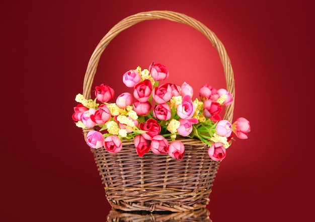 Bouquet of beautiful artificial flowers in wicker basket on red background