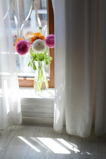 Photo bouquet of beautiful bright ranunculus flowers in glass vase indoors