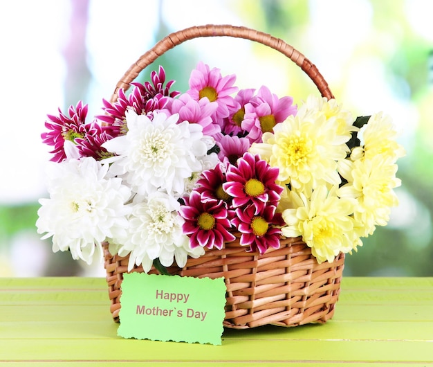 Bouquet of beautiful chrysanthemums in wicker basket on table on bright background