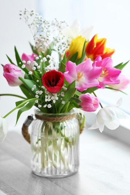 Bouquet of beautiful colorful tulips in glass vase on windowsill indoors