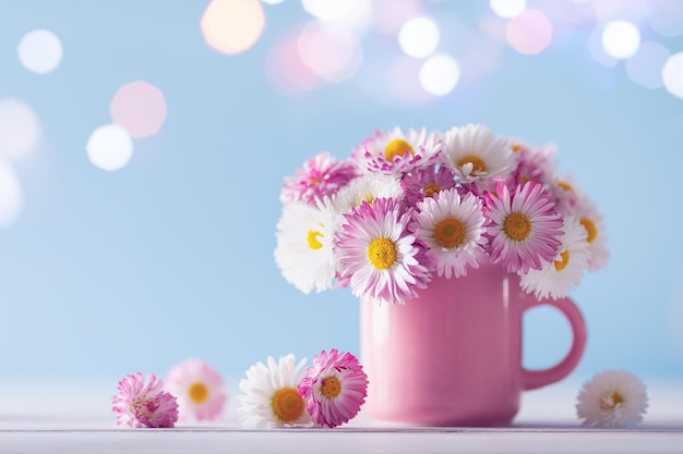 Bouquet of beautiful English daisy in pink cup against sparkle lights background Template of greeti