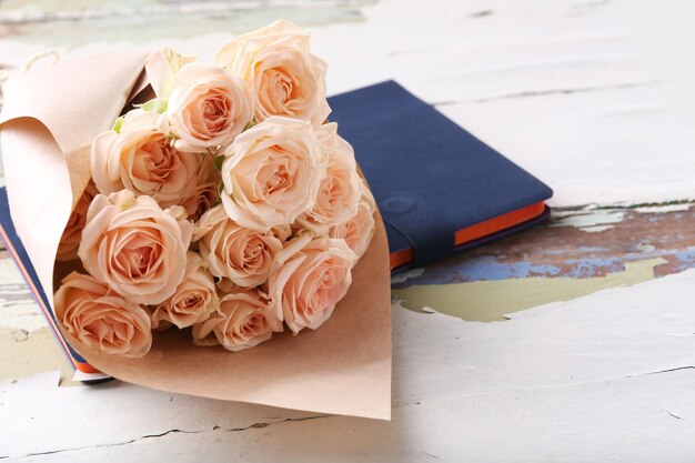 Photo bouquet of beautiful fresh roses with notebook on wooden table closeup