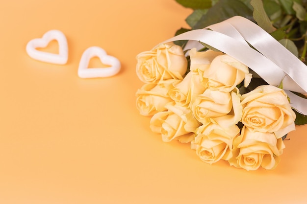 A bouquet of beautiful peach roses with a satin ribbon and two white hearts on a peach background Selective focus