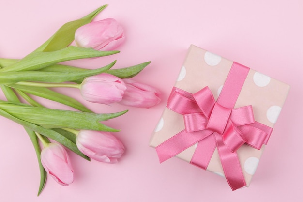 A bouquet of beautiful pink tulips flowers and a gift box on a trendy pink background Spring holidays top view