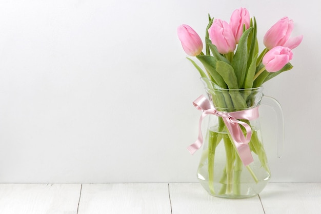 Bouquet of beautiful pink tulips flowers in a vase on a white wooden table Spring holidays free space