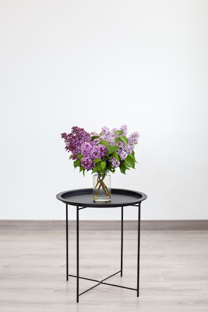 Bouquet of beautiful spring lilac flowers in vase on black vintage coffee table, home decor. Interior Design.