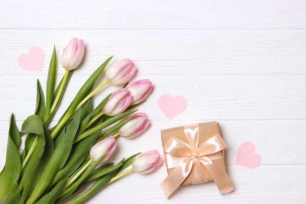 A bouquet of beautiful tulips and a gift on a wooden background top view