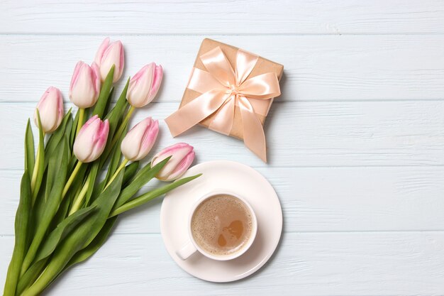 A bouquet of beautiful tulips and a gift on a wooden background top view