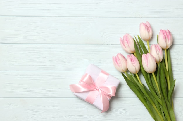 A bouquet of beautiful tulips and a gift on a wooden background top view