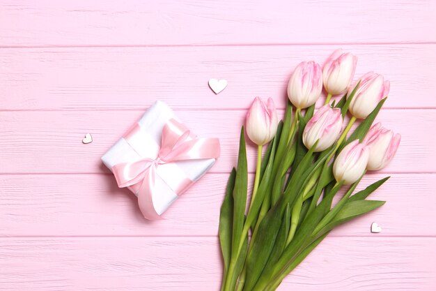 A bouquet of beautiful tulips and a gift on a wooden background top view
