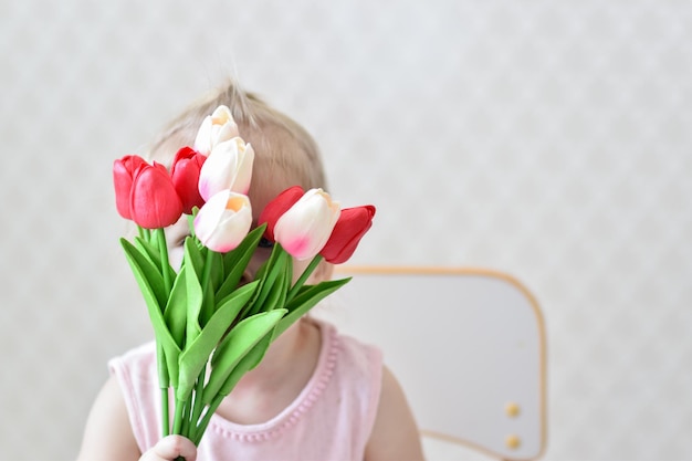 A bouquet of beautiful tulips in the hands of a child who is hiding behind a bouquet The concept of Mother's Day Women's Day copy space