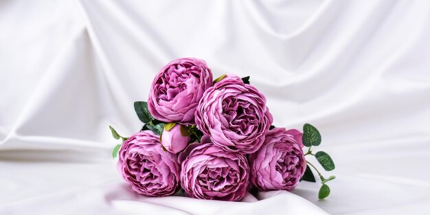 Photo bouquet of beautiful violet peonies on white silk fabric background copy space greeting card