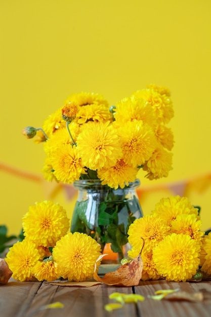 Bouquet of beautiful yellow chrysanthemums on wood table on yellow background.