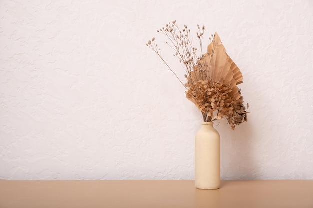 Bouquet of beige dried flowers and paper palms in a beige vase on white background Copy space