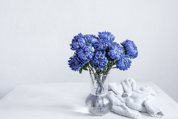 A bouquet of blue chrysanthemums in a glass vase and a knitted element on a white background, copy space.