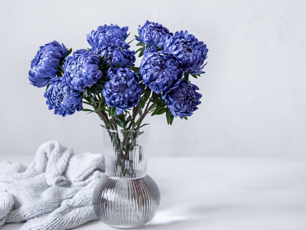 A bouquet of blue chrysanthemums in a glass vase and a knitted element on a white background, copy space.