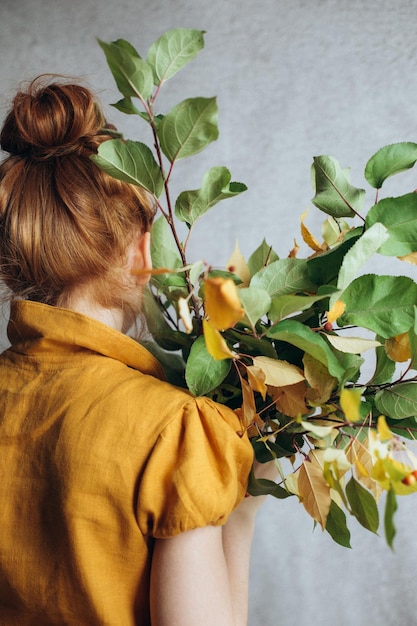 A bouquet of branches of an autumn tree in the hands of a red-haired girl