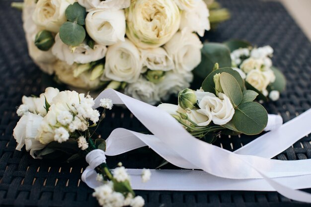 Bouquet of bride and boutonniere with white roses and white ribbons on a dark background Wedding accessories