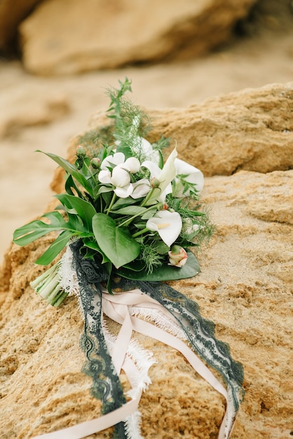 Bouquet of a bride from feces and roses lies on a sandstone stone on the seashore