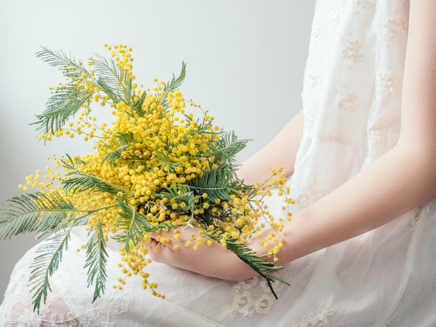 Bouquet of bright, yellow flowers in the hands of a young woman in a white dress