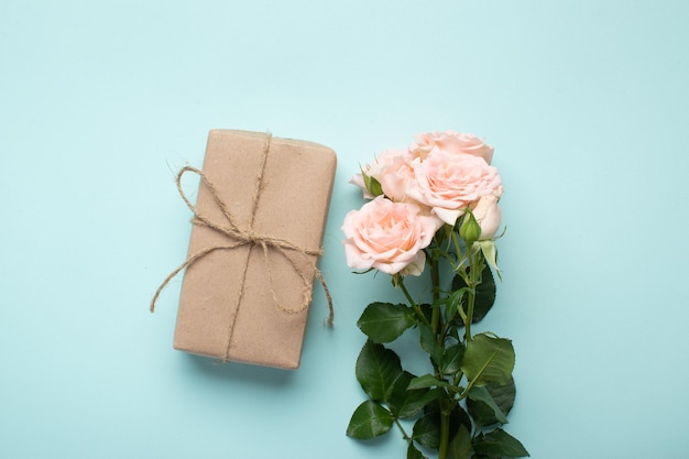 A bouquet of bush roses and a gift in kraft paper on a light blue background