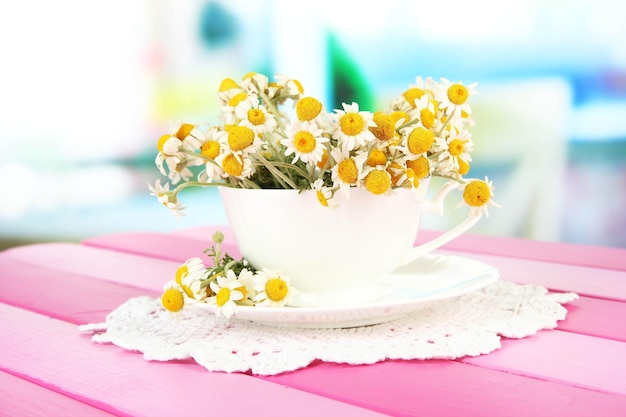 Bouquet of chamomile flowers in cup on bright background