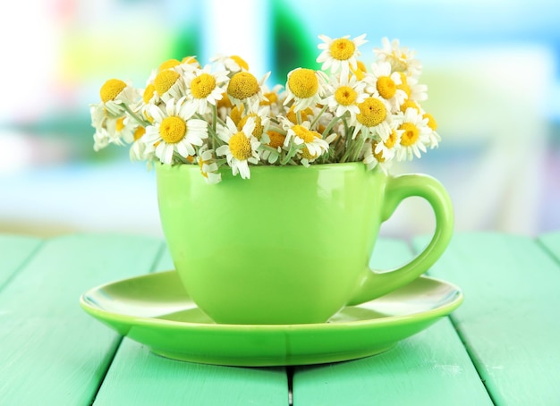 Bouquet of chamomile flowers in cup on bright background